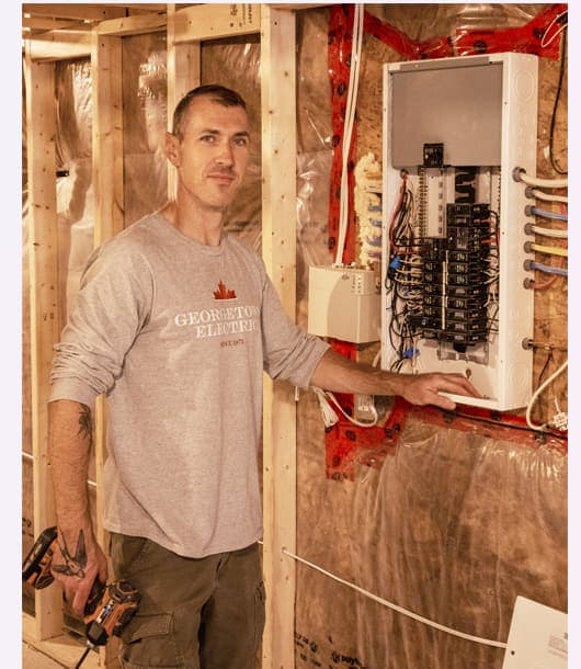 Electrician beside a newly installed, labelled breaker panel in a framed basement
