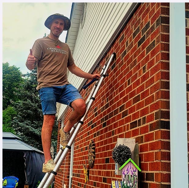 Electrician on a ladder during exterior electrical work on a brick home