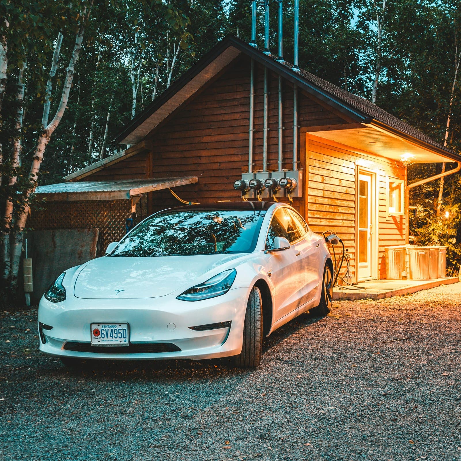 Electric vehicle charging beside a rural workshop at dusk
